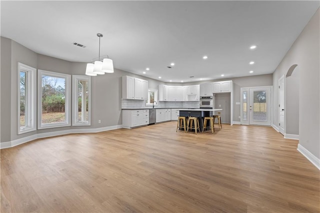 unfurnished living room with arched walkways, light wood-type flooring, a wealth of natural light, and recessed lighting