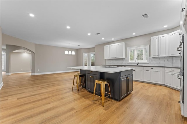 kitchen featuring visible vents, arched walkways, a breakfast bar, a center island, and white cabinetry