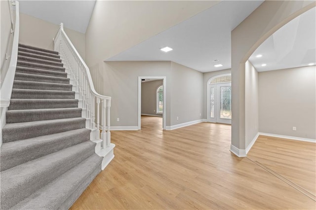 entryway featuring stairs, light wood finished floors, arched walkways, and baseboards