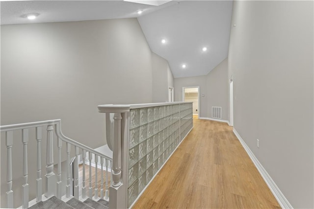 hallway featuring light wood finished floors, baseboards, visible vents, high vaulted ceiling, and recessed lighting