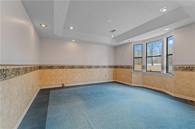 spare room with a wainscoted wall, dark colored carpet, and a textured ceiling