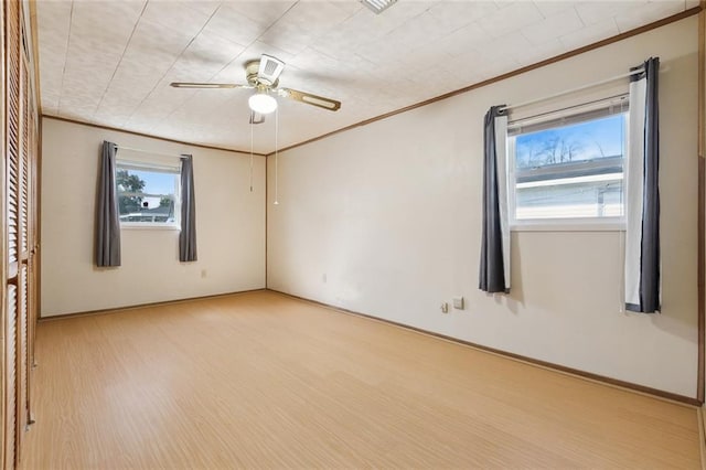 spare room with baseboards, light wood finished floors, a ceiling fan, and crown molding