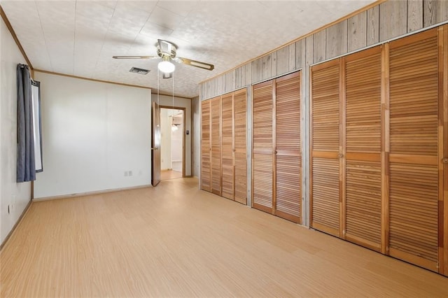 unfurnished bedroom featuring wood finished floors, visible vents, baseboards, multiple closets, and ornamental molding