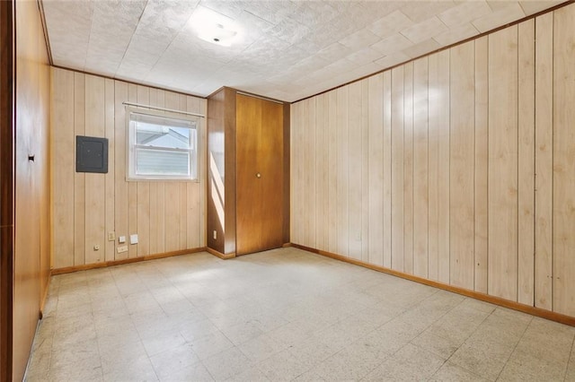 spare room with baseboards, electric panel, wooden walls, and light floors