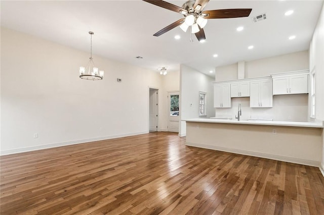 kitchen with pendant lighting, white cabinetry, dark hardwood / wood-style floors, ceiling fan with notable chandelier, and kitchen peninsula