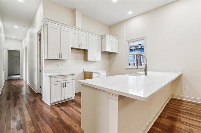 kitchen with white cabinetry, dark hardwood / wood-style floors, kitchen peninsula, and sink