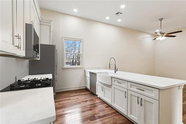 kitchen with sink, stainless steel dishwasher, kitchen peninsula, hardwood / wood-style floors, and white cabinets