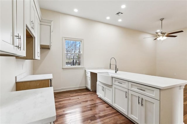 kitchen with sink, ceiling fan, wood-type flooring, white cabinets, and kitchen peninsula