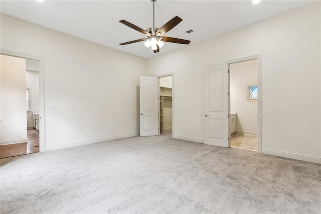 unfurnished bedroom featuring connected bathroom, a walk in closet, light colored carpet, and ceiling fan