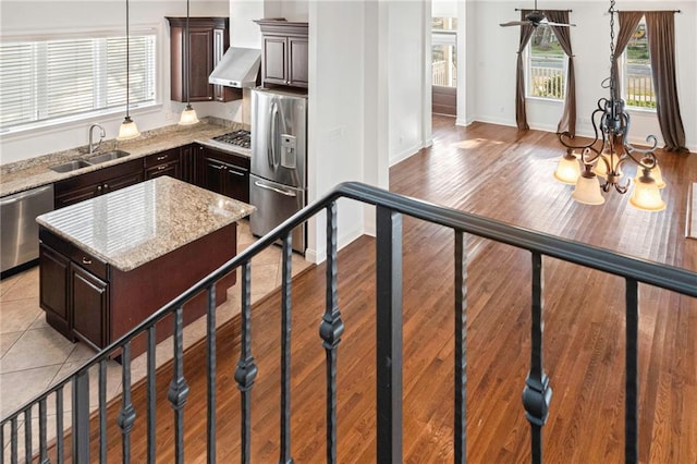 kitchen featuring appliances with stainless steel finishes, sink, a center island, light stone countertops, and dark brown cabinets