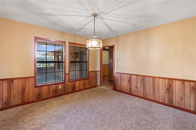 spare room with carpet, a textured ceiling, and wood walls