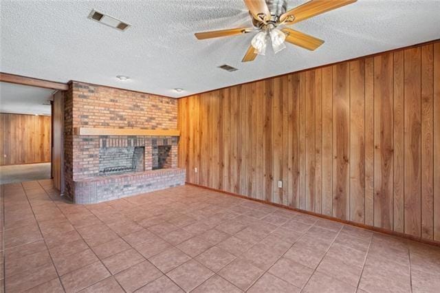 unfurnished living room featuring ceiling fan, a textured ceiling, a brick fireplace, and wood walls