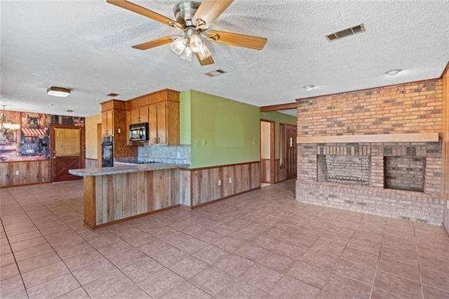 kitchen featuring a textured ceiling, a brick fireplace, kitchen peninsula, brick wall, and black appliances