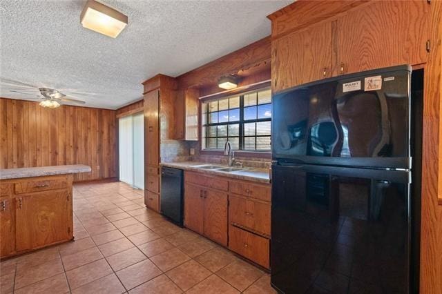 kitchen featuring sink, wood walls, a textured ceiling, light tile patterned floors, and black appliances