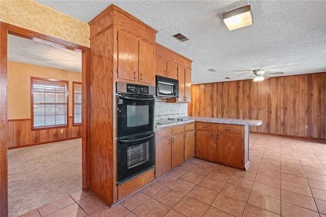 kitchen featuring light tile patterned flooring, wood walls, a textured ceiling, kitchen peninsula, and black appliances