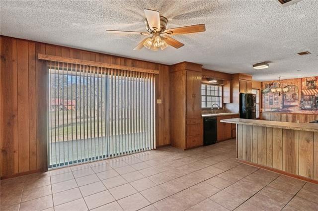 kitchen featuring sink, hanging light fixtures, black appliances, ceiling fan with notable chandelier, and wood walls