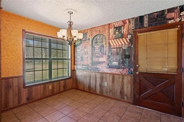 unfurnished dining area with an inviting chandelier, tile patterned floors, a textured ceiling, and wood walls