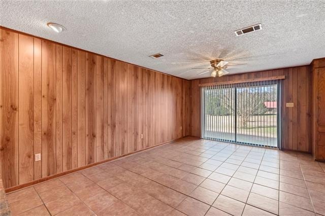 tiled empty room with a textured ceiling, ceiling fan, and wood walls