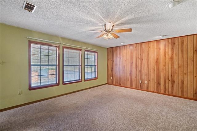 carpeted spare room with a textured ceiling, ceiling fan, and wood walls