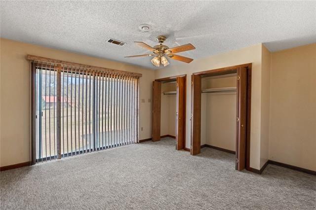 unfurnished bedroom with multiple closets, ceiling fan, light carpet, and a textured ceiling