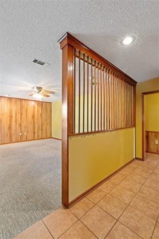 hallway with light carpet, a textured ceiling, and wood walls