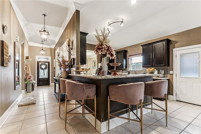 kitchen featuring dark brown cabinetry, a kitchen bar, light tile patterned floors, ornamental molding, and kitchen peninsula