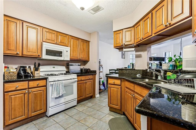 kitchen with sink, white appliances, light tile patterned floors, dark stone countertops, and a textured ceiling