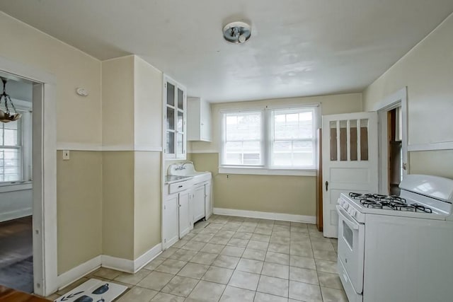 kitchen featuring white cabinetry, sink, light tile patterned flooring, and white gas range oven