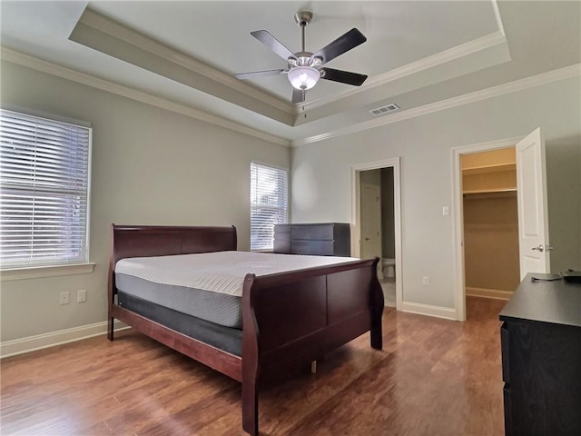 bedroom featuring a tray ceiling, wood finished floors, visible vents, and baseboards