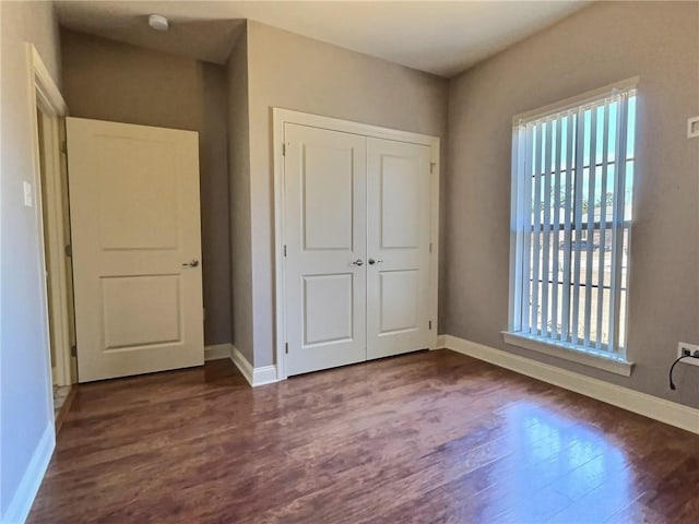 unfurnished bedroom with dark wood-style floors, baseboards, and a closet