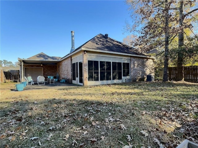 rear view of property featuring a garage, brick siding, fence, and a sunroom