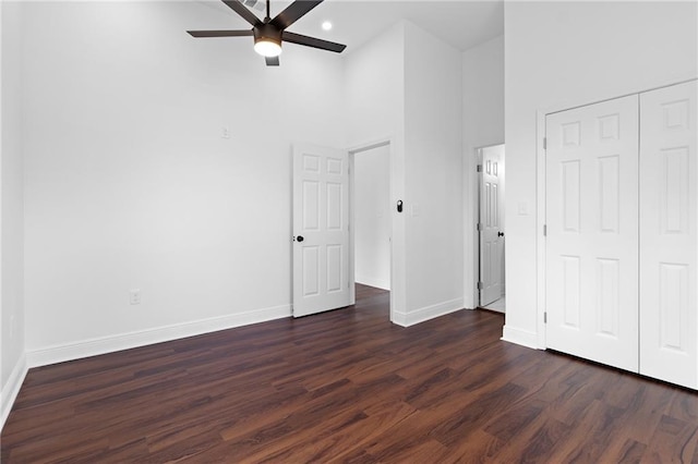 unfurnished bedroom featuring dark wood-type flooring, ceiling fan, a closet, and a high ceiling