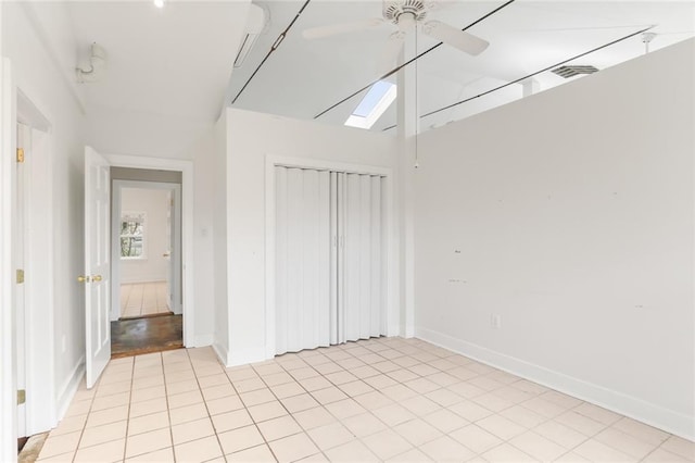 unfurnished bedroom with light tile patterned floors, vaulted ceiling with skylight, a closet, and ceiling fan