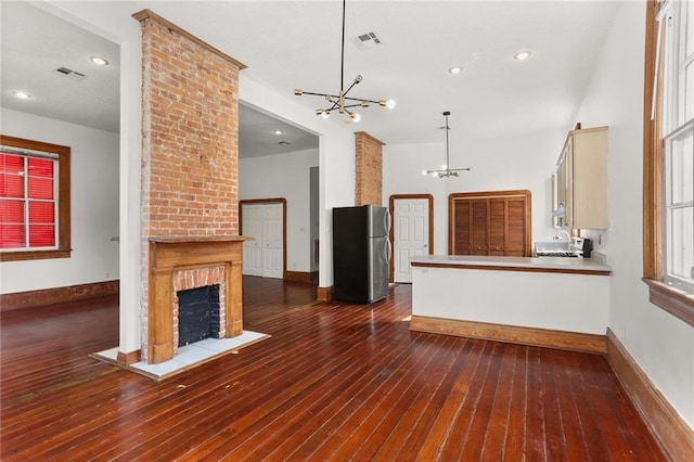 unfurnished living room with a brick fireplace, dark wood-type flooring, and a chandelier