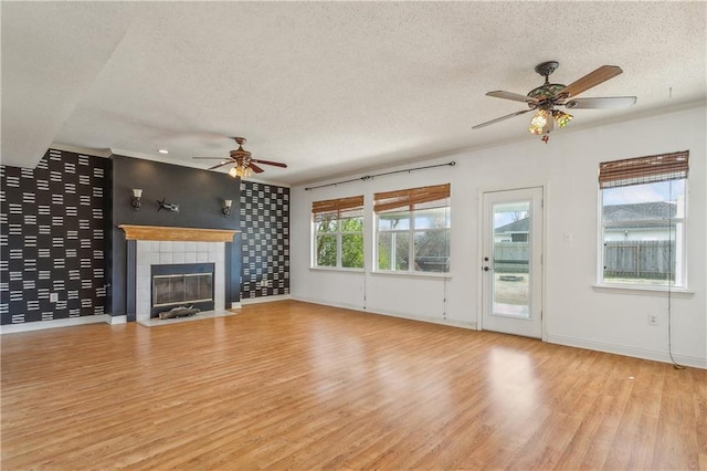 unfurnished living room with a textured ceiling, ornamental molding, ceiling fan, a fireplace, and light hardwood / wood-style floors