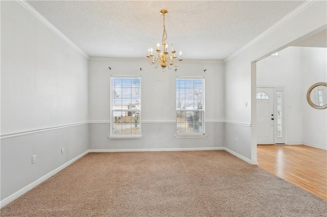 carpeted empty room with ornamental molding, a textured ceiling, and a chandelier