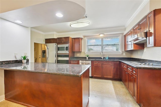 kitchen featuring dark stone countertops, a sink, appliances with stainless steel finishes, under cabinet range hood, and crown molding