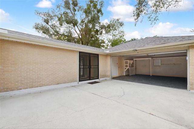 back of house with an attached garage, brick siding, driveway, and roof with shingles