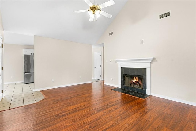 unfurnished living room featuring a tiled fireplace, high vaulted ceiling, ceiling fan, and light hardwood / wood-style flooring