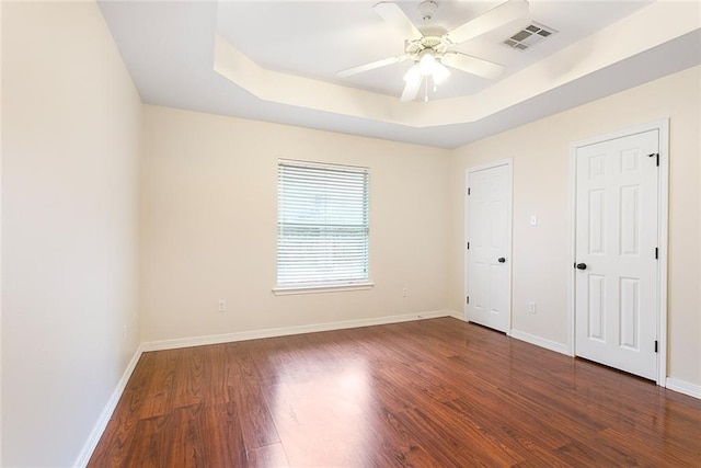 unfurnished bedroom with dark hardwood / wood-style floors, ceiling fan, and a raised ceiling