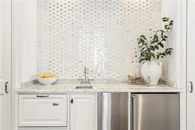 bar with sink, white cabinets, stainless steel refrigerator, and decorative backsplash