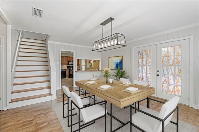 dining area featuring visible vents, light wood-style floors, ornamental molding, french doors, and stairway