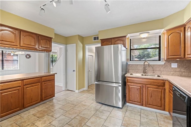 kitchen featuring black dishwasher, brown cabinetry, a sink, and freestanding refrigerator