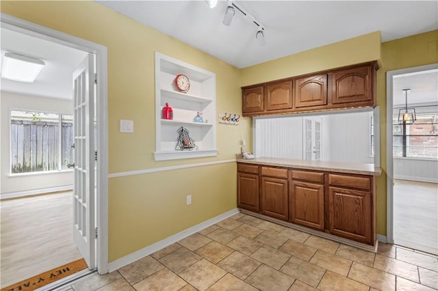 kitchen featuring baseboards, built in features, brown cabinetry, and light countertops