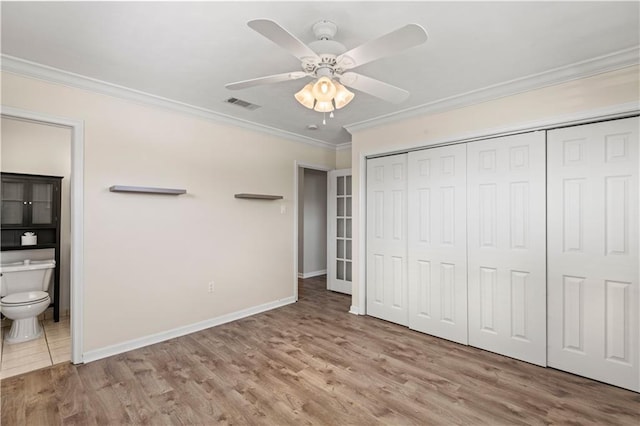 unfurnished bedroom featuring baseboards, visible vents, ensuite bath, ornamental molding, and wood finished floors