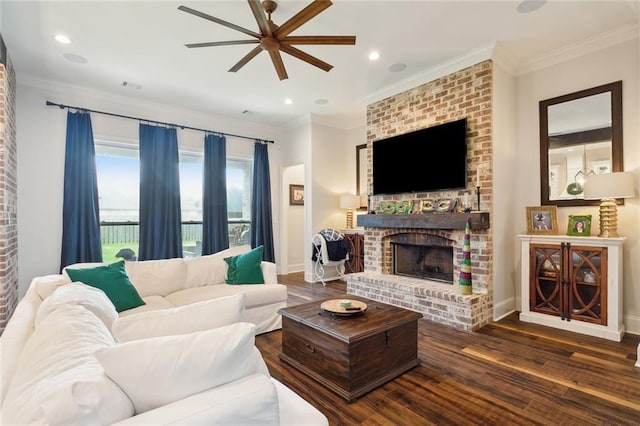 living room with a brick fireplace, crown molding, dark wood-type flooring, and ceiling fan