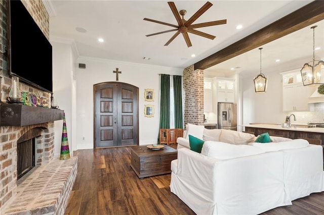 living room featuring sink, crown molding, beam ceiling, a fireplace, and dark hardwood / wood-style flooring