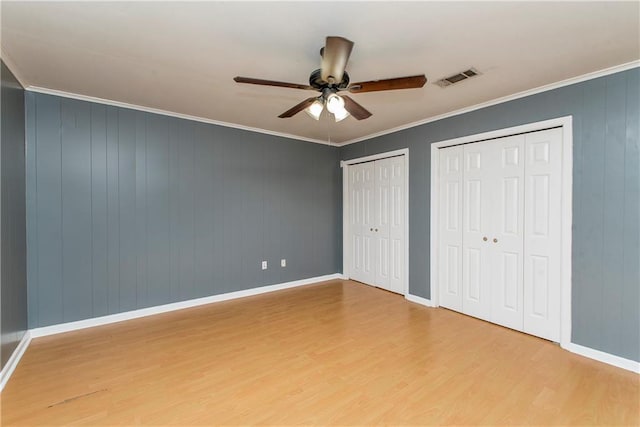 unfurnished bedroom with crown molding, ceiling fan, multiple closets, and light wood-type flooring