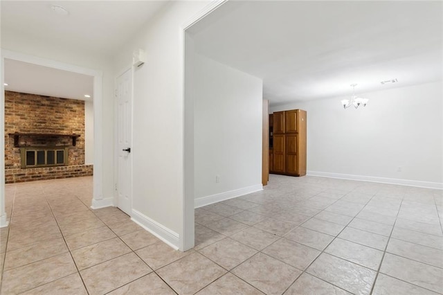 empty room featuring a chandelier, a brick fireplace, and light tile patterned floors