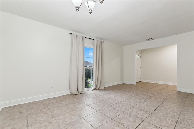 tiled spare room featuring a chandelier